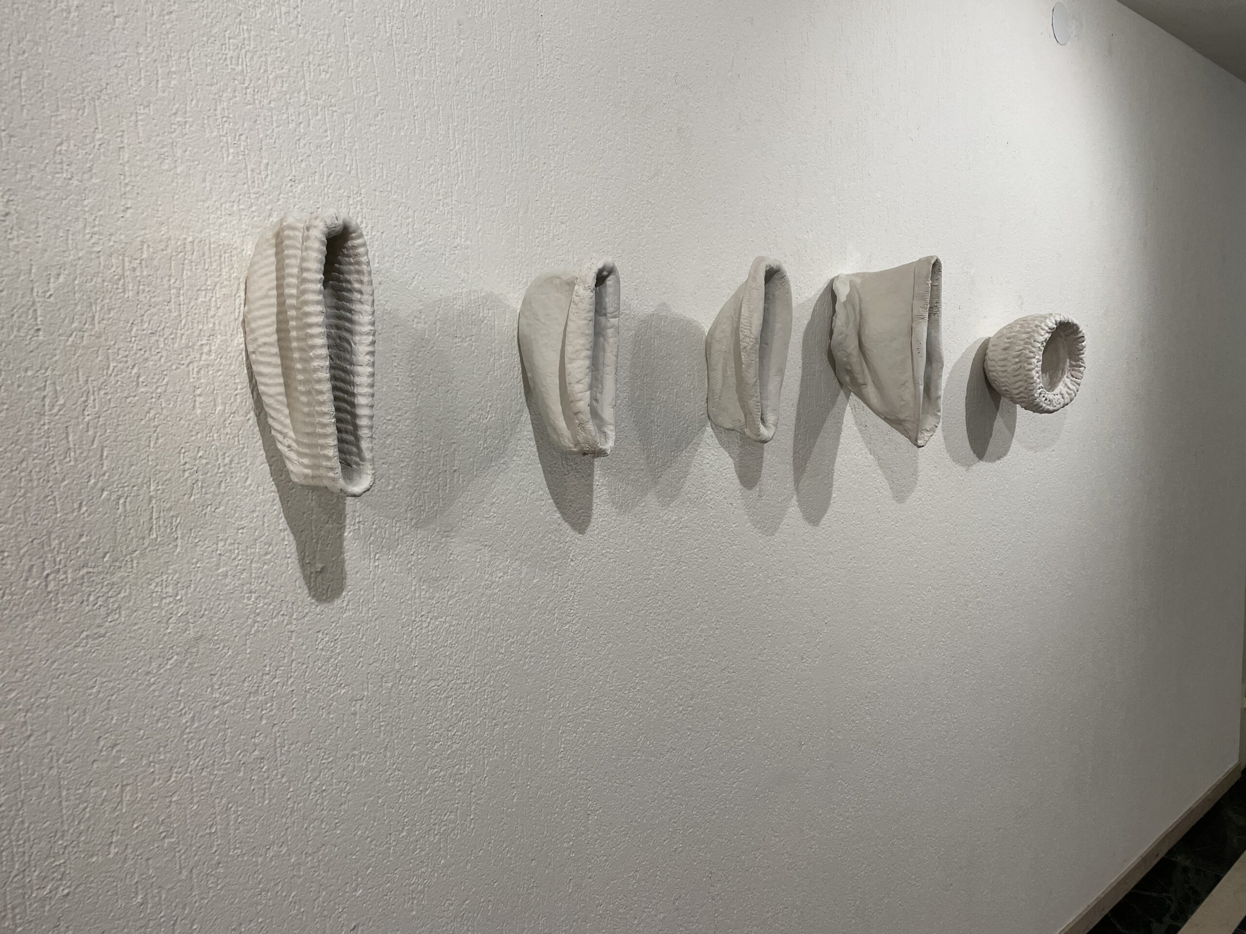 Fünf eingegeipste Mützen hängen mot der offnung nach vorne an der Wand.